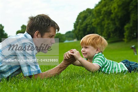 Father and son lying on lawn in park and playing