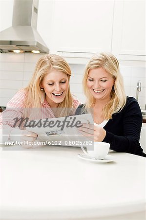 Two young women reading newspaper in kitchen