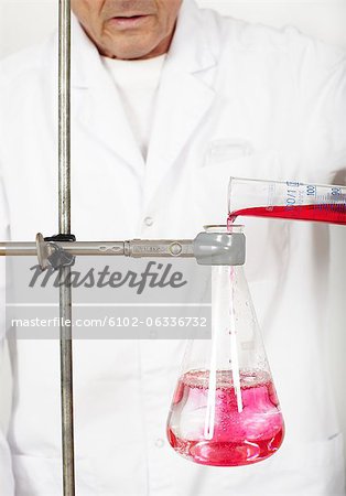 Scientist pouring chemical into beaker, mid section