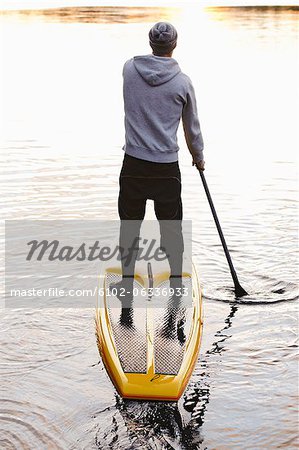 Man rowing paddle board in water, rear view