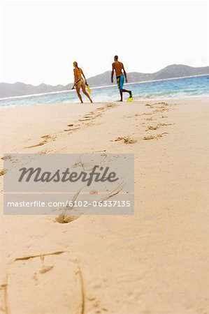 Diving flipper prints on sand, mid adult couple in background