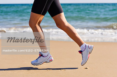 Young woman running on beach, low section, Algarve, Portugal