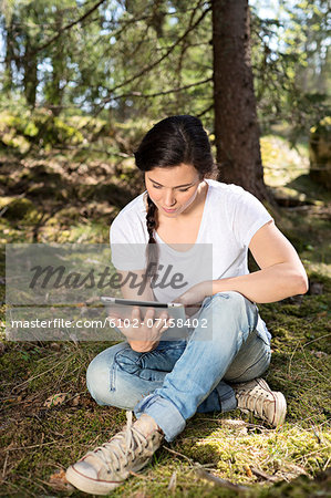 Young woman in forest using digital tablet