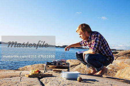 Man having grill on cliff, Bohuslan, Sweden