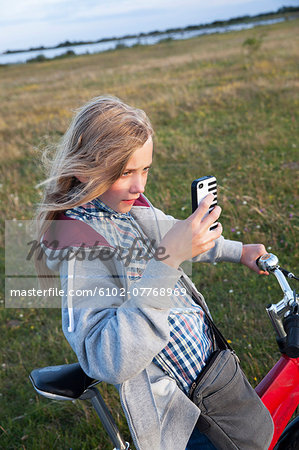 Girl on bike taking picture with her cell phone, Sweden