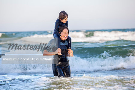 Mother carrying son on shoulders in sea
