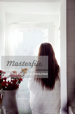 Woman wrapped in blanket standing looking through window