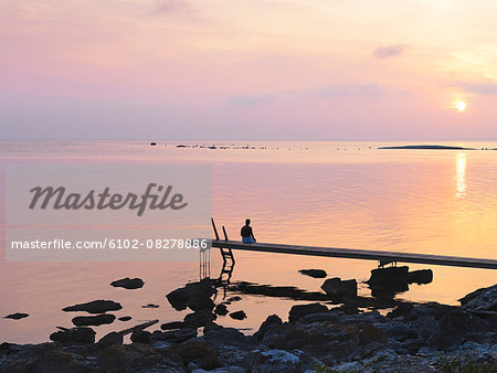 Man sitting on jetty at sunset Man sitting on jetty at sunset