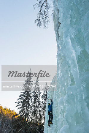 Man climbing up on frozen waterfall