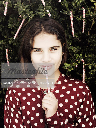 Portrait of girl eating candy cane from tree