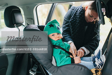 Mother with putting baby son in car seat