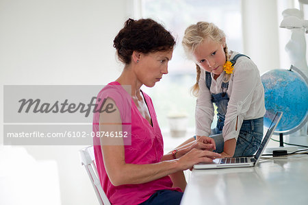 Woman working on laptop while girl is watching her