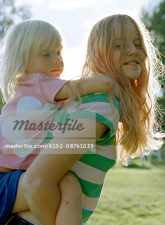 Young girl carrying sister giving piggyback ride Stock Photo