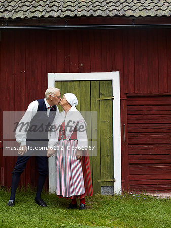 Senior couple wearing traditional costumes kissing in front of house, Dalarna, Sweden
