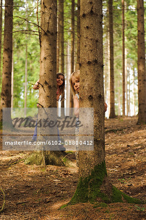 Two girls standing behind trees in forest