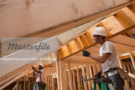 Hispanic carpenters working on roof rafters at a house under construction