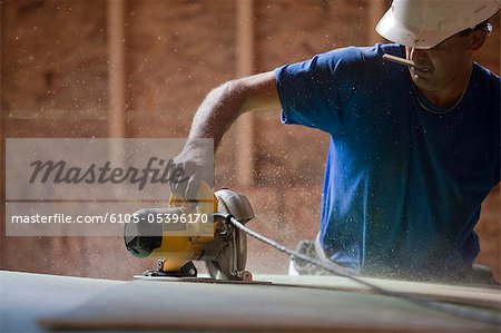 Hispanic carpenter using a circular saw on the roofing sheathing at a house under construction