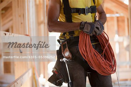 Hispanic carpenter coiling electrical power cord at a construction site