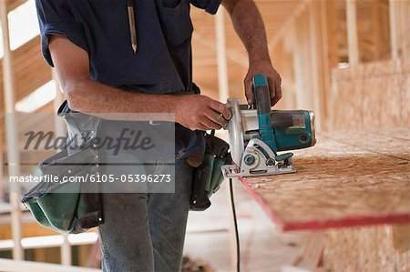 Hispanic carpenter using a circular saw on roof panel at a house under construction
