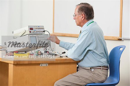 Professor adjusting oscilloscope triggering level in electronics classroom