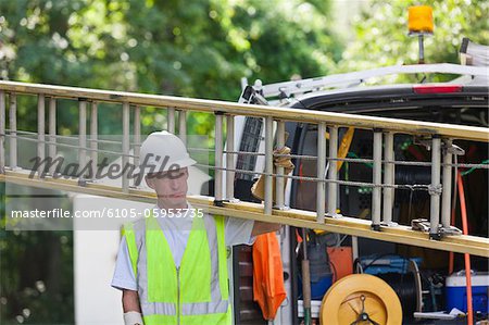 Communications worker carrying a ladder from truck to make installation