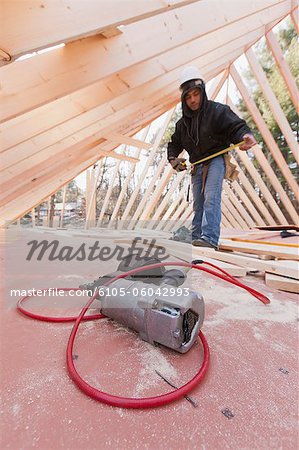 Close-up of a nail gun with a carpenter using measuring tape in the background