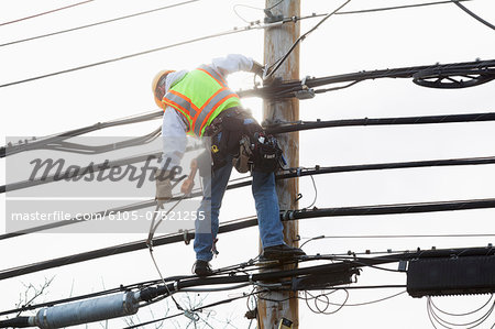Communications worker on a power pole preparing to strap safety harness to support cable