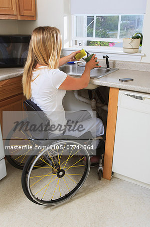 Woman with spinal cord injury in her accessible kitchen washing dishes