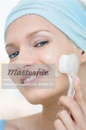 Young Woman face looking at the camera, cleaning her cheeks with a brush, close-up (studio)