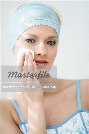 Young Woman face using a cleansing cotton on her cheek, close-up (studio)