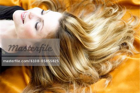 Portrait of a young woman lying, long hair on yellow textil fabric