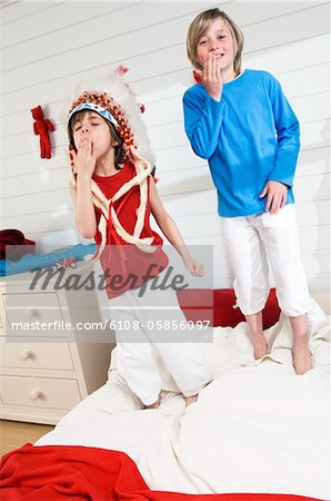 2 boys playing indians standing onbed