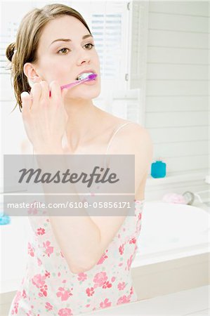 Young woman in nightgown brushing her teeth in front of bathroom mirror