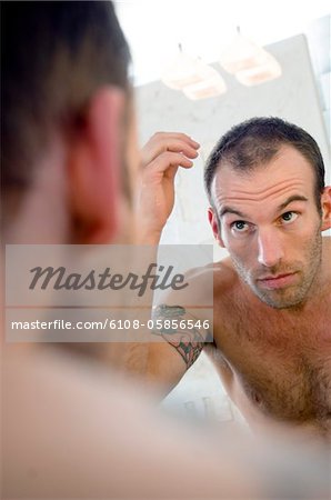 Tattooed man, barechested, looking in bathroom mirror