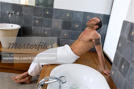 Tattooed man, barechested, resting on tub edge