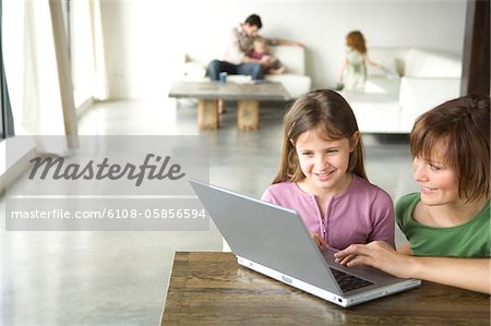 Woman and little girl using laptop computer, man and 2 children in the background