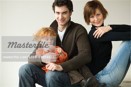 Couple and little girl sitting on the floor, looking at the camera