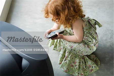 Little girl crouching in front of television, holding remote control, elevated view