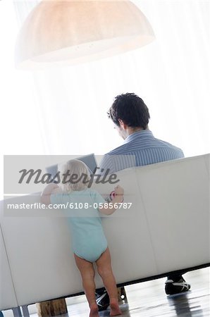 Rear view of little boy watching man using laptop computer