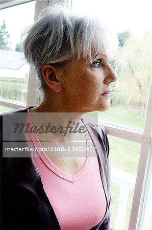 Thinking senior woman looking through a window