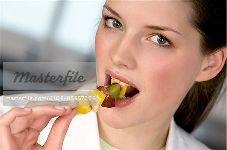 Portrait of a young woman eating a fruit skewer