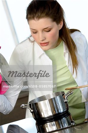 Young woman in the kitchen, lifting saucepan lid