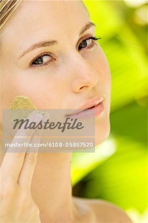 Young woman applying face scrub cream on her face, outdoors