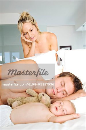 Young woman looking at man and baby sleeping, indoors