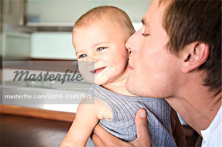 Portrait of father and son in kitchen, man kissing his baby, indoors
