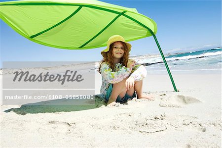 Little girl sitting on the beach under large green leaf, outdoors