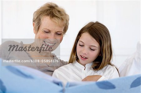 Senior woman and little girl in bed, looking at photograph album