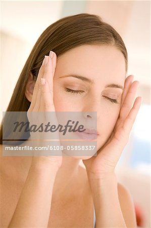 Portrait of a young woman shut eyes, hands on her cheeks, indoors