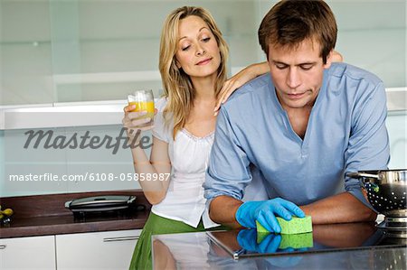 https://image1.masterfile.com/getImage/6108-05858987em-young-woman-laughing-at-man-using-sponge-in-kitchen-stock-photo.jpg