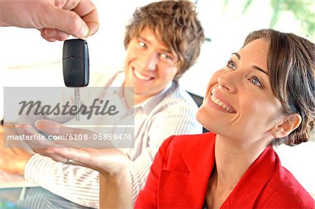 Car dealer handing car key to customer, smiling